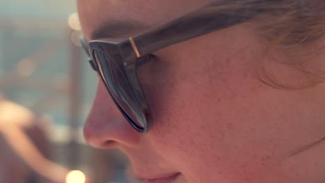 a woman with strawberry blonde or ginger hair, wearing sunglasses, sits on a moving boat, sketching what she sees in front of her
