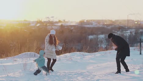 Aktive-Familie-Wirft-Bei-Sonnenuntergang-Weißen-Schnee-Gegen-Dächer