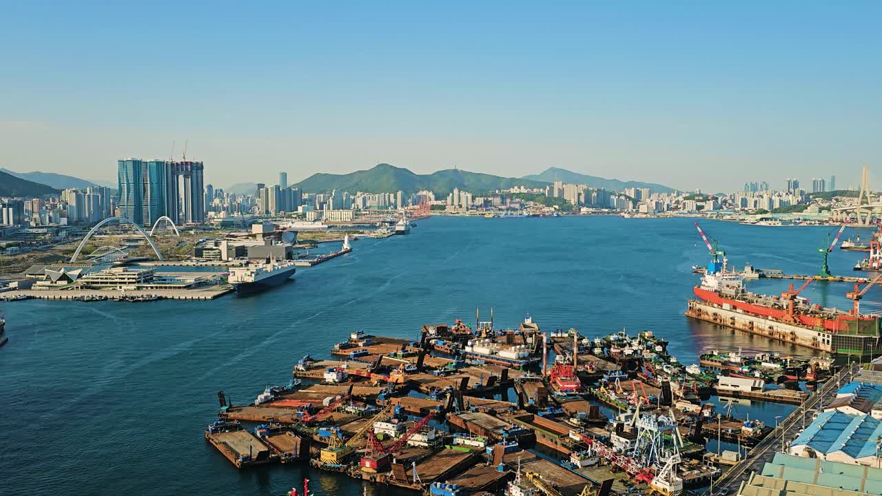 Aerial view of Busan port showcasing docked ships, industrial harbor, city skyline, and coastal buildings - zoom in
