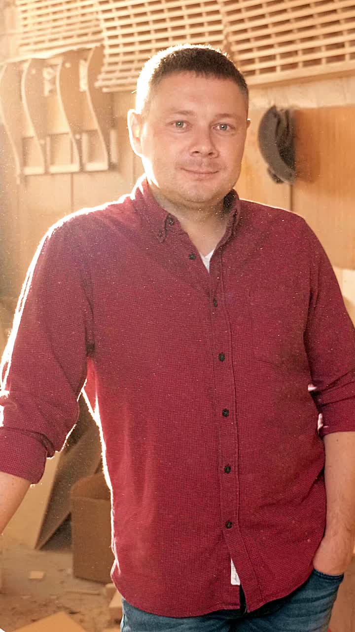 Skilled craftsman in a workshop, wearing a red shirt, stands confidently with tools and wood materials in the background, showcasing dedication to craftsmanship and artistry