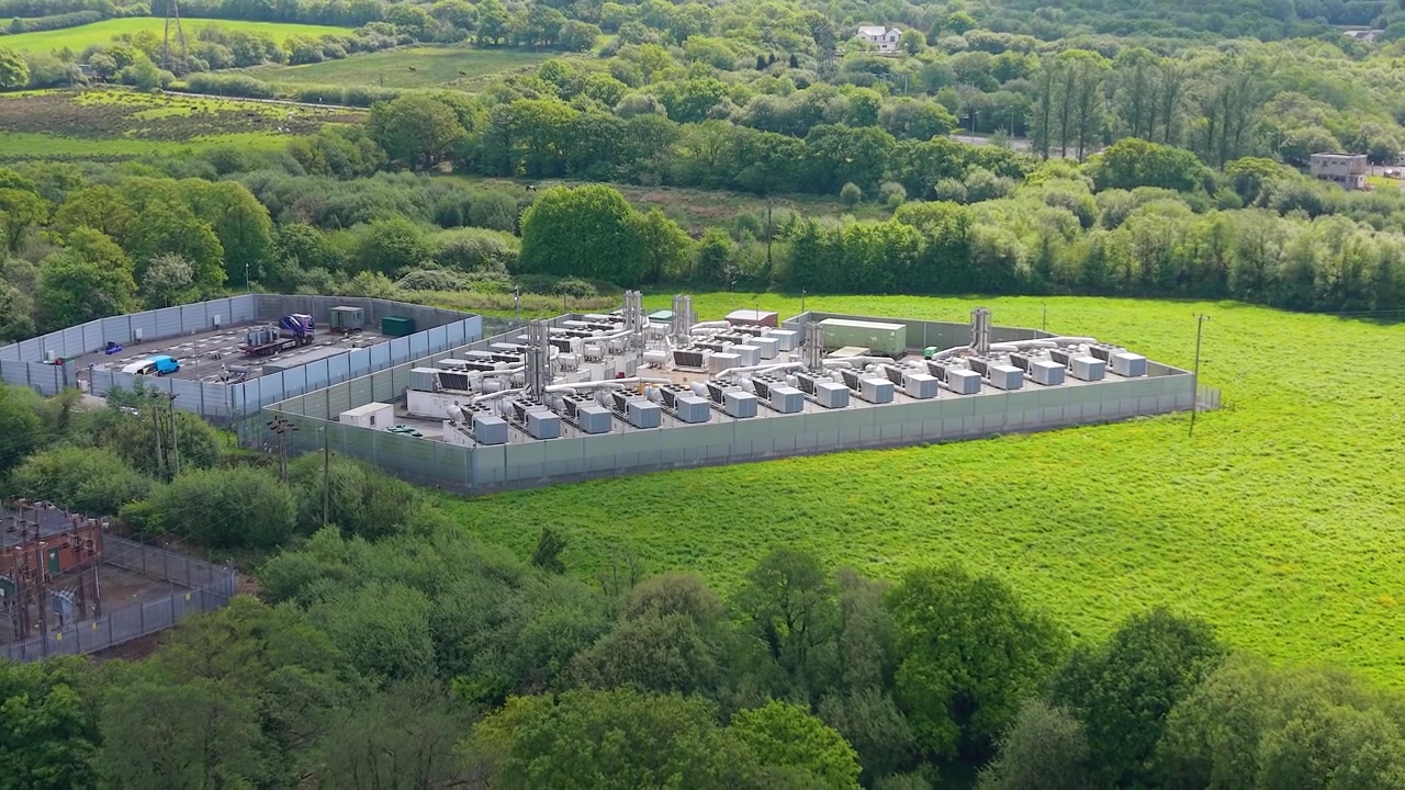 Retreating Aerial of modern gas peaking plant with exhaust stacks, generators, cooling systems. BESS Battery Storage Under Construction. Rapid-response electricity to the grid during peak demand.