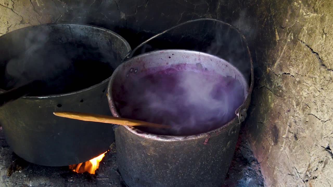 Two blackened pots boiling over open fire, filled with purple colored water and alpaca wool in a traditional Quechua dyeing process in Sacred Valley