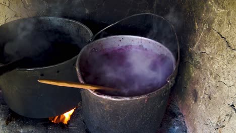 two blackened pots boiling over open fire, filled with purple colored water and alpaca wool in a traditional quechua dyeing process in sacred valley