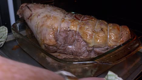 a joint of pork in a glass baking dish is picked up and put inside the oven