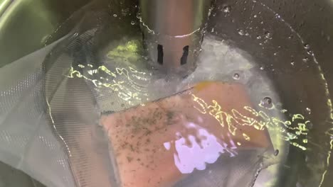 closing up to slow cooking salmon fillet. bubbles coming out of a slow cooker machine. salmon fillet compressed airtight with vacuum machine cooking in the pot in slow motion.