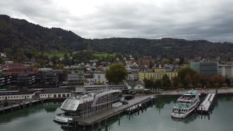 Vista-Aérea-De-La-Histórica-Bregenz,-Se-Puede-Ver-El-Ferry-En-El-Puerto-En-Un-Feliz-Día-Nublado-De-Otoño,-Al-Fondo-Las-Colinas-Con-Bosques-Llenos-De-Tranquilidad,-Vorarlberg,-Austria,-Europa