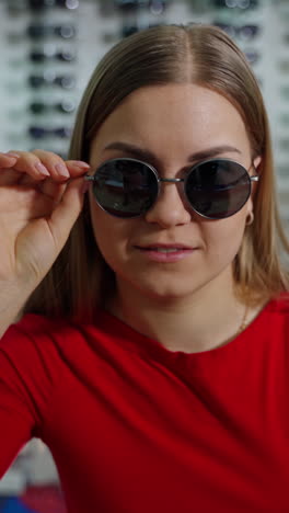 beautiful woman trying on stylish sunglasses. long-haired girl in modern black sunglasses posing on camera at optical store. vertical video