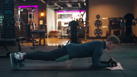 a caucasian well-built man is doing plank exercise in a modern gym - side view