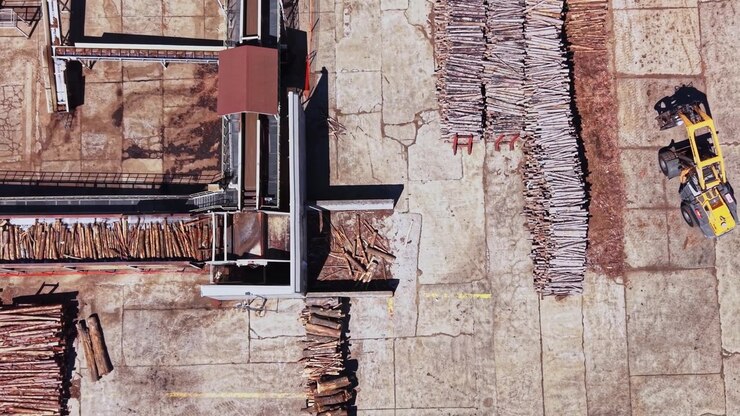 Cantiere edile mostra tronchi di legno impilati a terra.