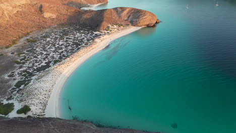 cinematic drone shot of balandra beach, passing over the red hills and turquoise waters, slowly tilting up