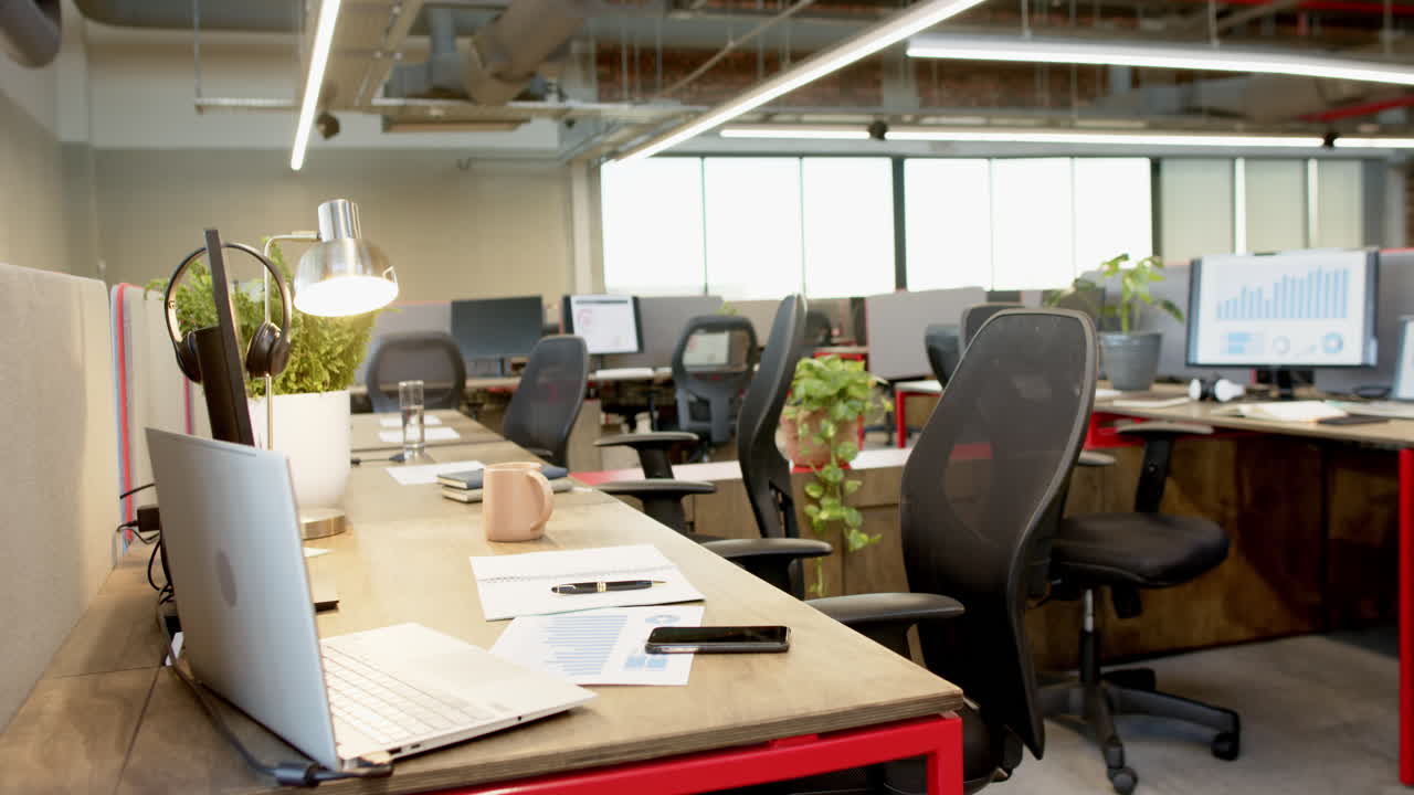Ufficio moderno vuoto con diverse postazioni di lavoro, sedie ergonomiche e ampie finestre.
