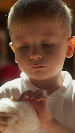 little boy with blond hair appetizingly eats bakery product with sausage on blurred background of market. toddler eats lunch standing in food area