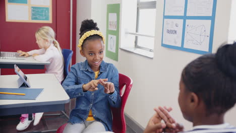 in school, girl using sign language to communicate with classmate in classroom