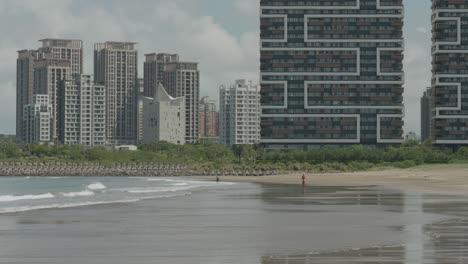 el agua del océano se extiende a través de las llanuras de arena de la playa de shalun con rascacielos detrás