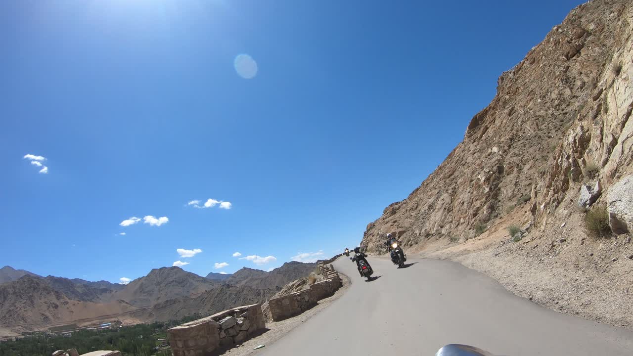 young couple riding bike in the hilly terrain of leh ladakh region heading towards shanti stupa with a bike ahead bikers point of view  blue sky and mountains