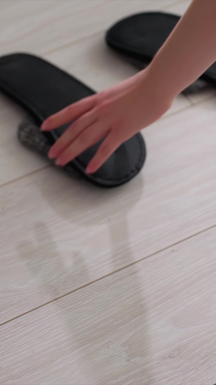 Shows hands picking up folded socks from white wooden floor. hand moves smoothly as each sock is picked and placed near black slippers emphasizing careful handling of laundry items