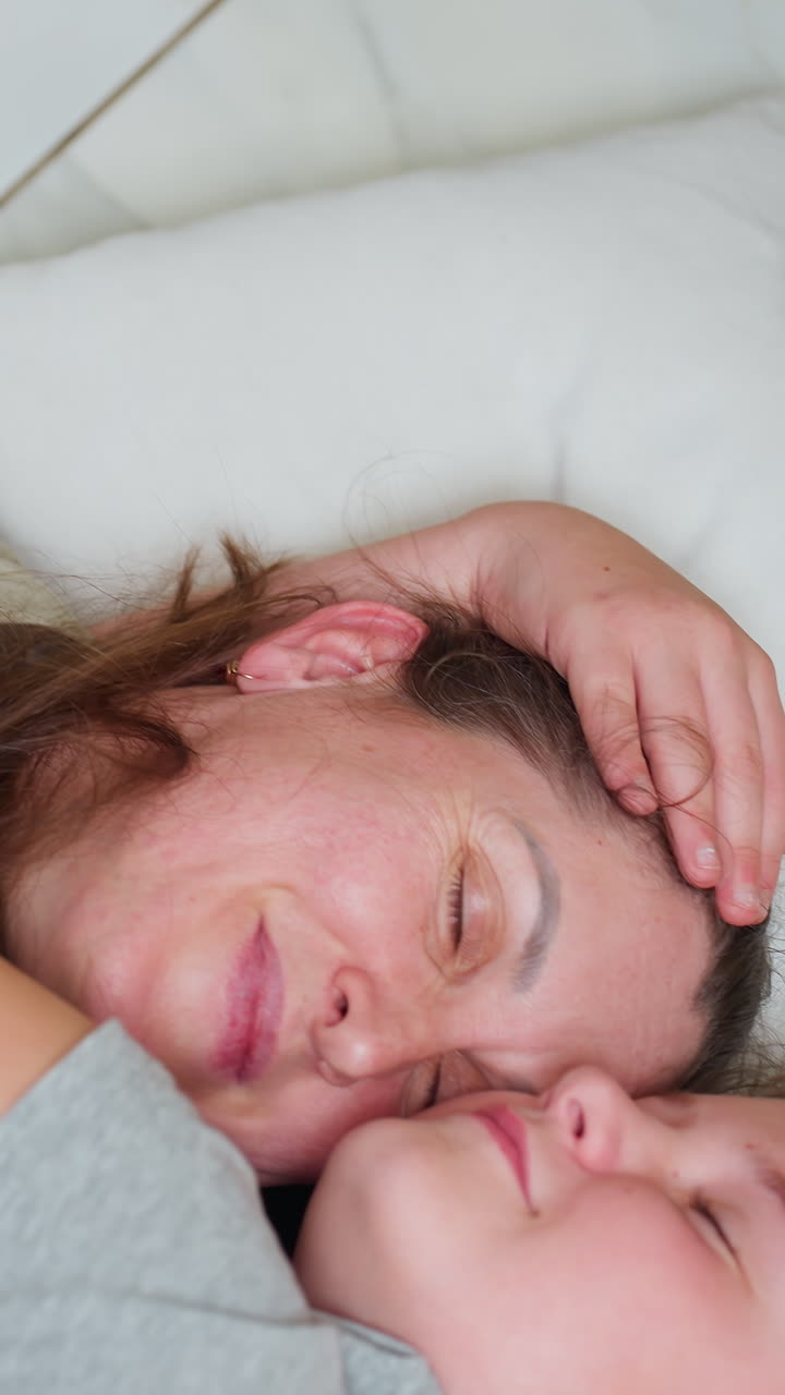 Madre blanca abrazando a su hijo en la cama, acogedor abrazo matutino con rostro pecoso y niño somnoliento, almohada suave y camiseta gris, mano suave en la cabeza, primer plano de un momento de cuidado maternal y vínculo silencioso, natural