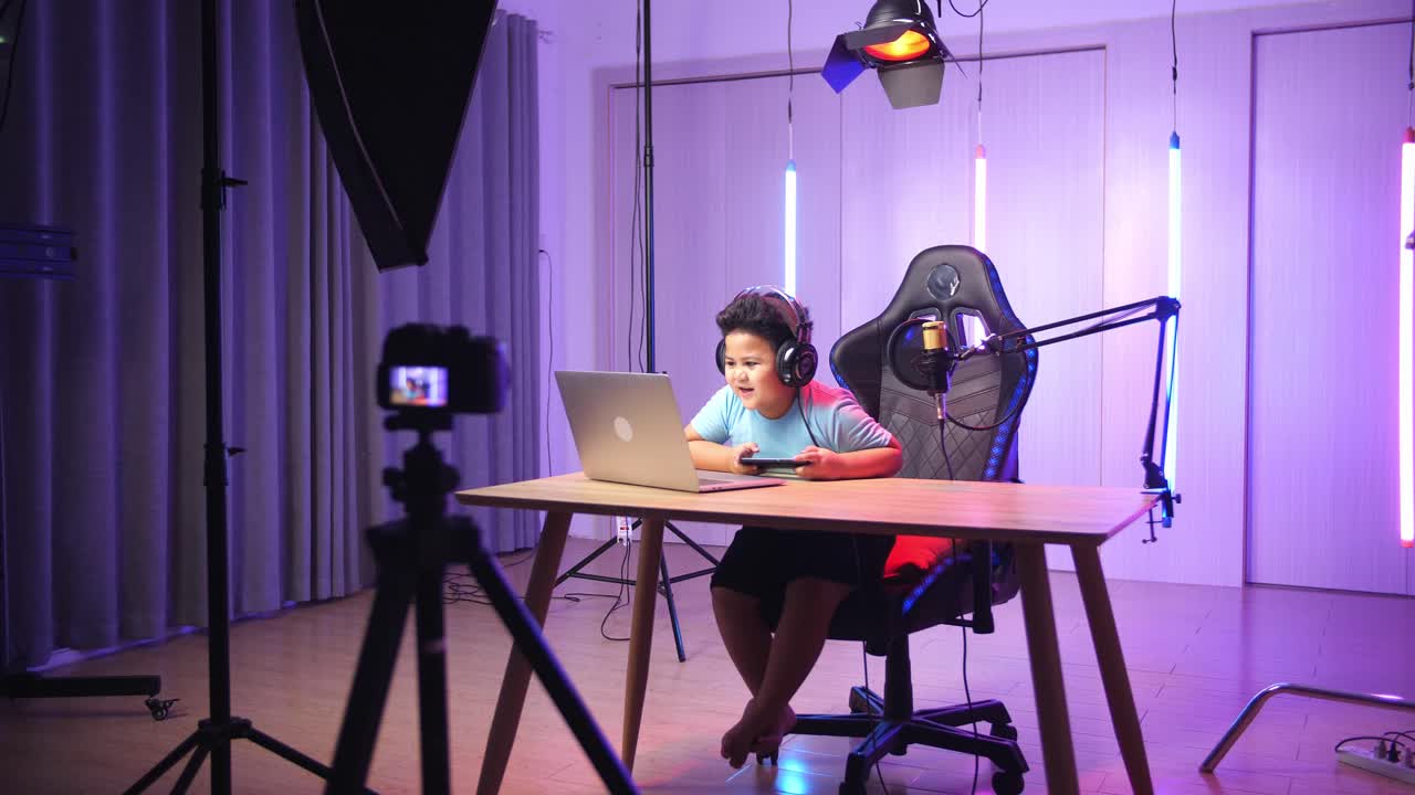 Asian Little Boy Holding Mobile Phone And Read Comment In Laptop Computer Then Talking To Camera While Live Stream, Professional Light Equipment