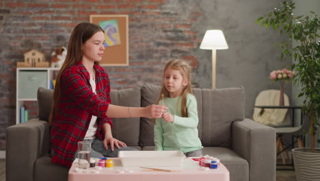 girl gives brush to elder sister preparing for ebru drawing