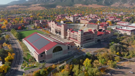 Aerial-pan-up-view-of-CU-Boulder-campus-and-Folsom-football-field-surrounded-by-green-and-yellow-fall-trees-with-the-rocky-flatiron-mountains-in-the-background-in-the-front-range-of-Colorado