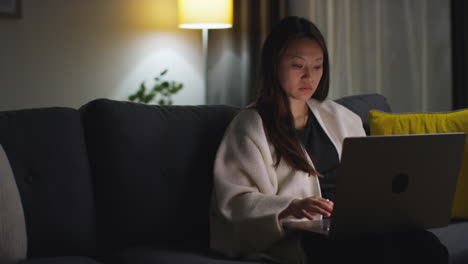 woman spending evening at home sitting on sofa with laptop computer looking at social media streaming or scrolling online 6