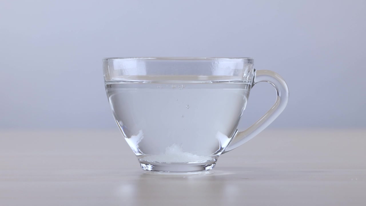 Primo piano di un cubetto di zucchero bianco che si scioglie lentamente in una tazza di vetro con acqua calda.