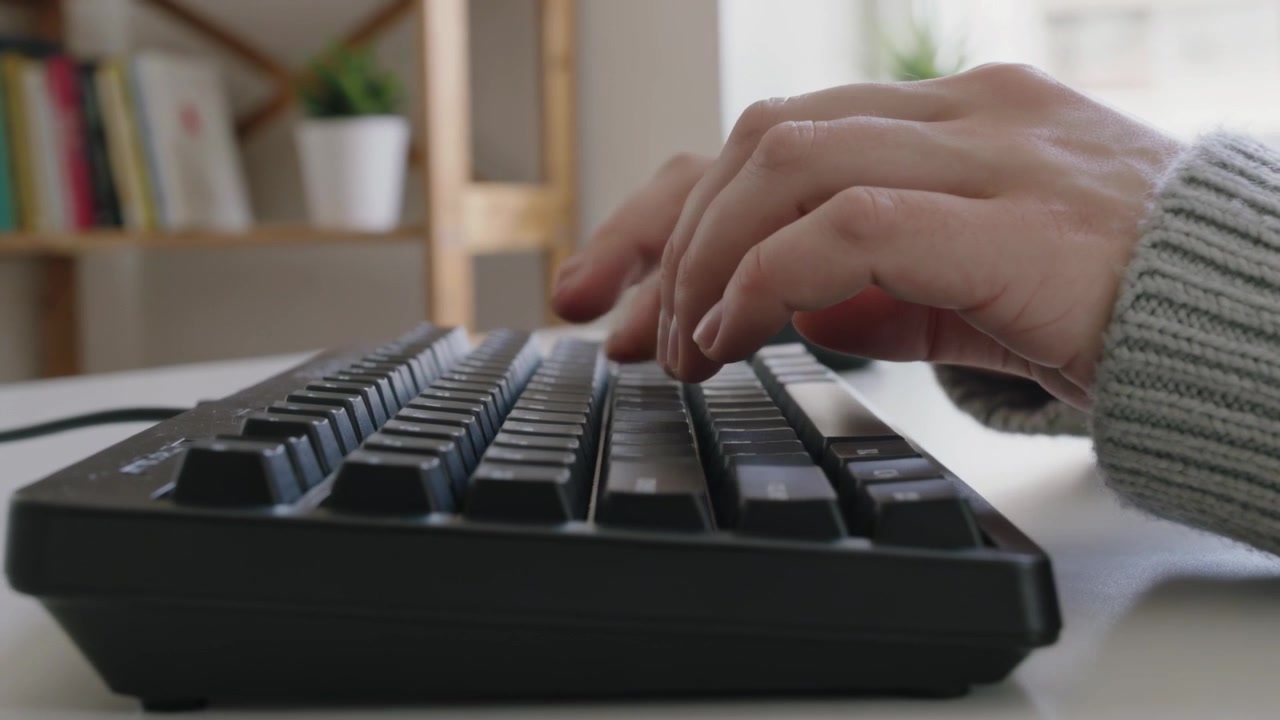 Typing hands wearing sweater starting after resting above keys, working on desk with black keyboard