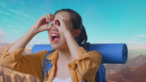 close up of asian female hiker with mountaineering backpack making binoculars gesture looking at something then saying wow while traveling at the top of mountain