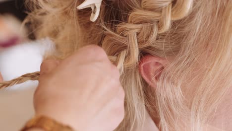 Woman-weaving-herringbone-braid-for-blonde-hair-bride-getting-ready