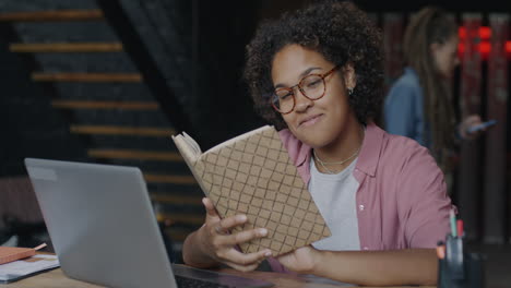 woman reading a book at a laptop