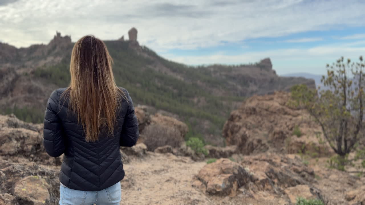 A woman with long brown hair admires the beauty of Roque Nublo on the island of Gran Canaria. Canary Islands.