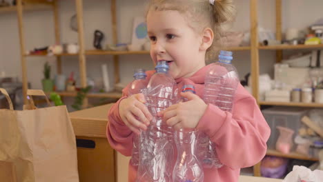 Kleines-Blondes-Mädchen,-Das-Plastikflaschen-In-Einer-Handwerkswerkstatt-Hält