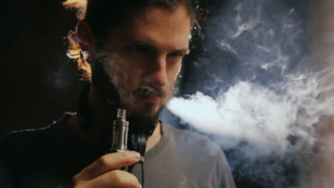 a young bearded man smoking an electronic cigarette smoke comes out beautifully in a beam of light