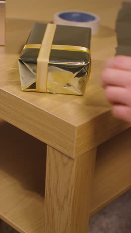 video vertical de un hombre envolviendo y poniendo un arco en un regalo o regalo en la mesa en casa