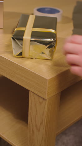 vertical video of man wrapping and putting bow on gift or present on table at home