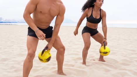 Diverse-male-and-female-athletes-doing-kettlebell-swing-exercise-on-beach