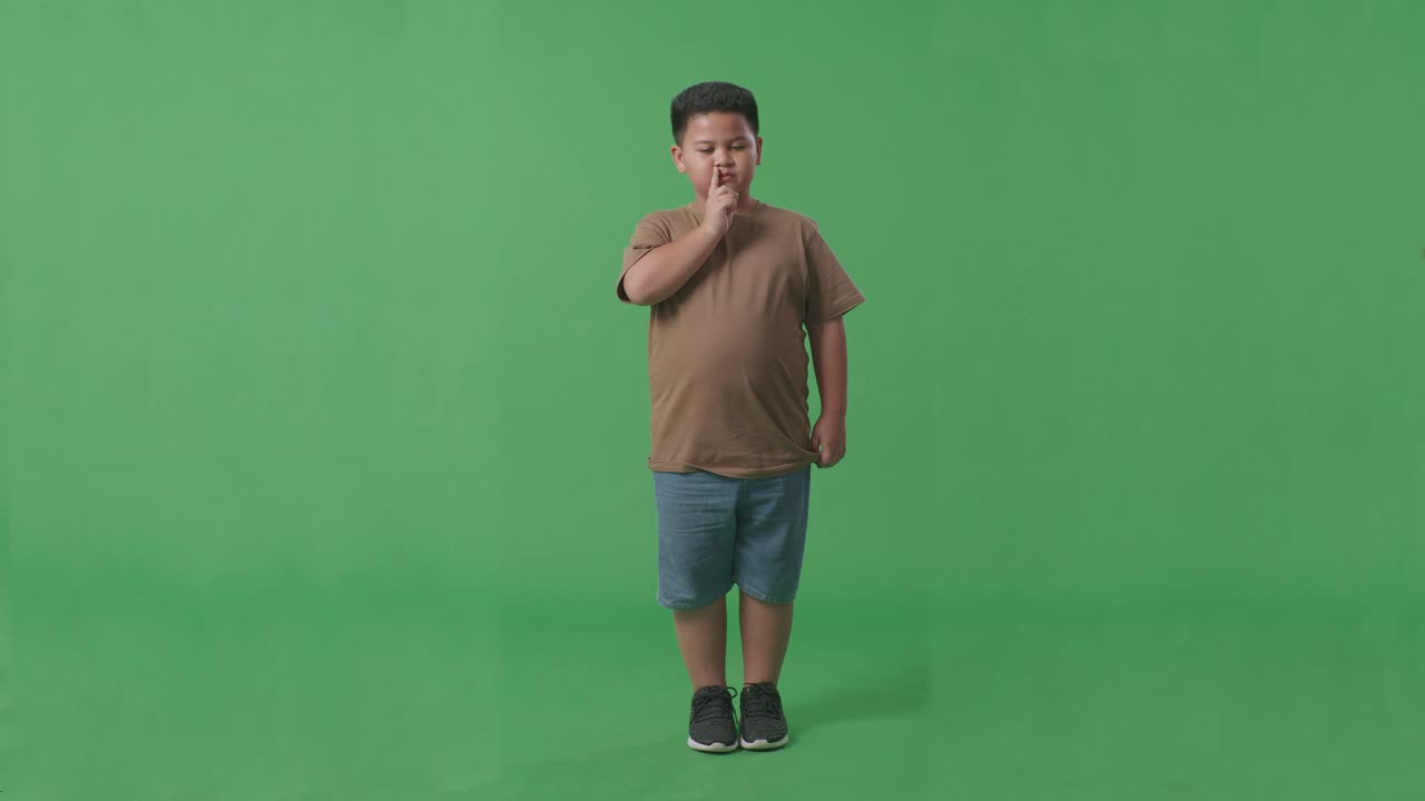 스튜디오에서 녹색 화면 배경에 침 제스처를 보여주는 아시아 소년의 전체 몸체