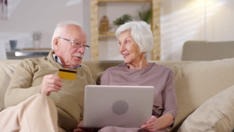 retired couple sitting on sofa at home and shopping online together