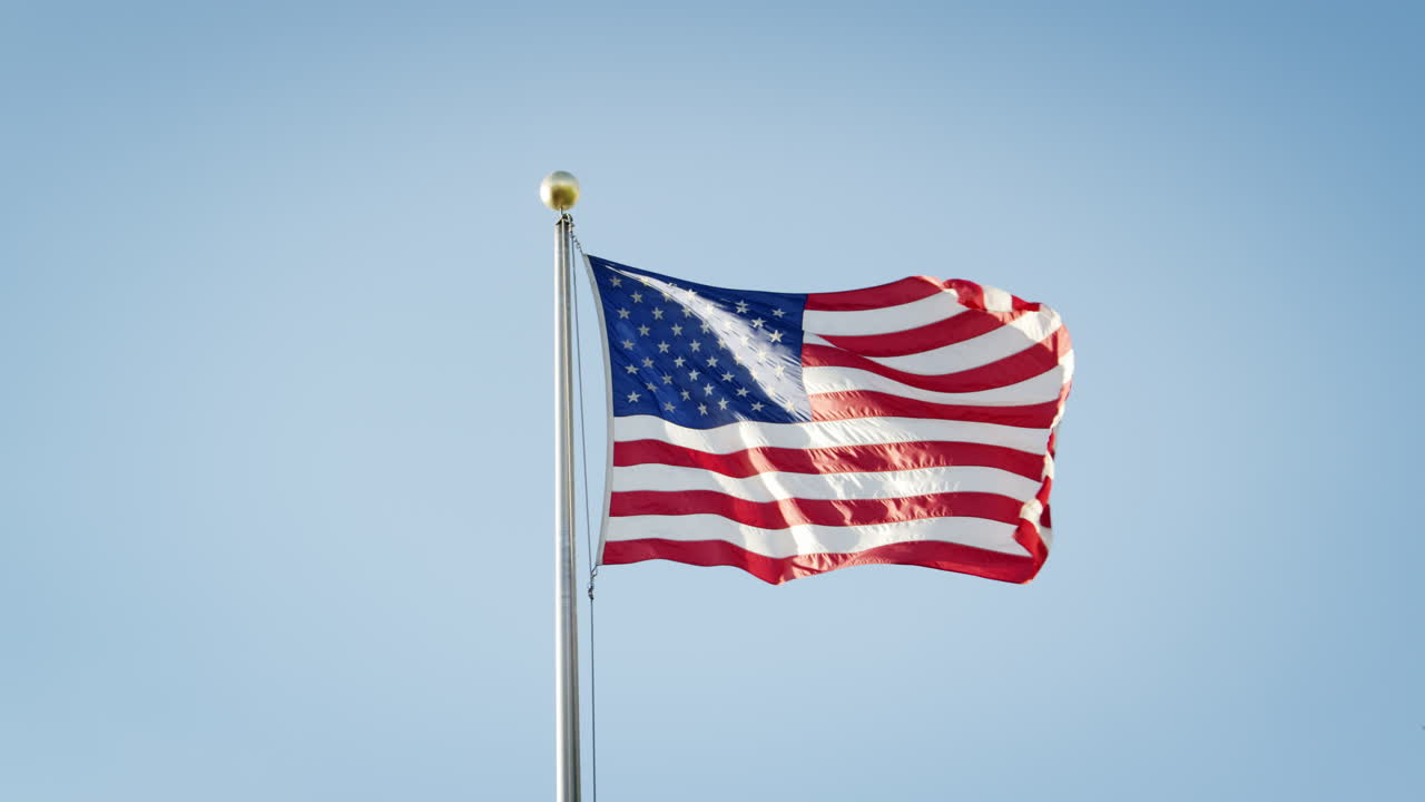 bandera estadounidense volando contra el cielo azul claro en cámara lenta