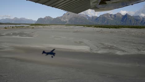 volando sobre campos fangosos en el paisaje de alaska, vista aérea desde un pequeño avión con sombra en tierra, punto de vista del pasajero