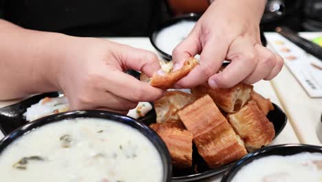 hands breaking dough sticks over congee bowl