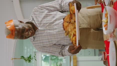 vertical video of grandfather carrying turkey as multi-generation family sit down to eat christmas meal together