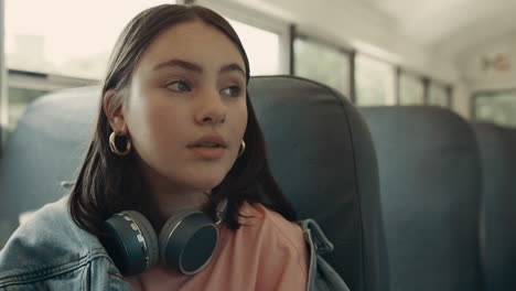 Portrait-thoughtful-girl-sitting-bus-with-headphones.-Schoolgirl-looking-window.