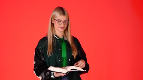 Estudiante-Bastante-Rubia-Pasando-Las-Páginas-Del-Libro,-Volteando-Las-Páginas,-Foto-De-Estudio-Con-Fondo-Rojo