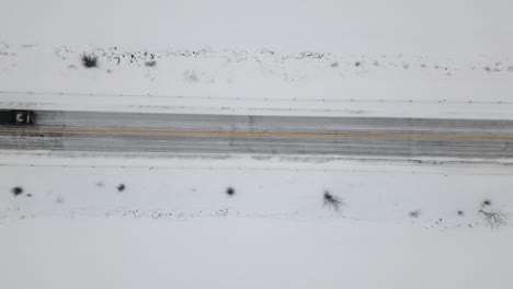 Una-Camioneta-Todoterreno-Negra-De-Arriba-Hacia-Abajo-Conduciendo-Bajo-Un-Disparo-Estático-De-Un-Dron-En-Una-Carretera-Cubierta-De-Nieve-En-Invierno