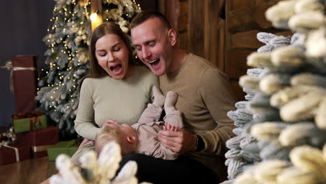 caucasian parents smile to their cute baby lying on dad's laps. loving family together at christmas holidays.