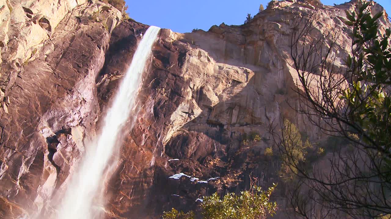 pan de ángulo bajo a través de una hermosa cascada en el parque nacional de yosemite mientras arroja un arco iris