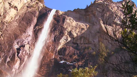 Low-angle-pan-across-a-beautiful-waterfall-in-Yosemite-National-park-as-it-casts-a-rainbow