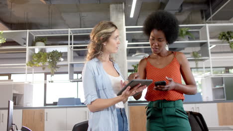 Diverse-creative-female-colleagues-in-discussion-using-tablet-and-smartphone-in-office,-slow-motion