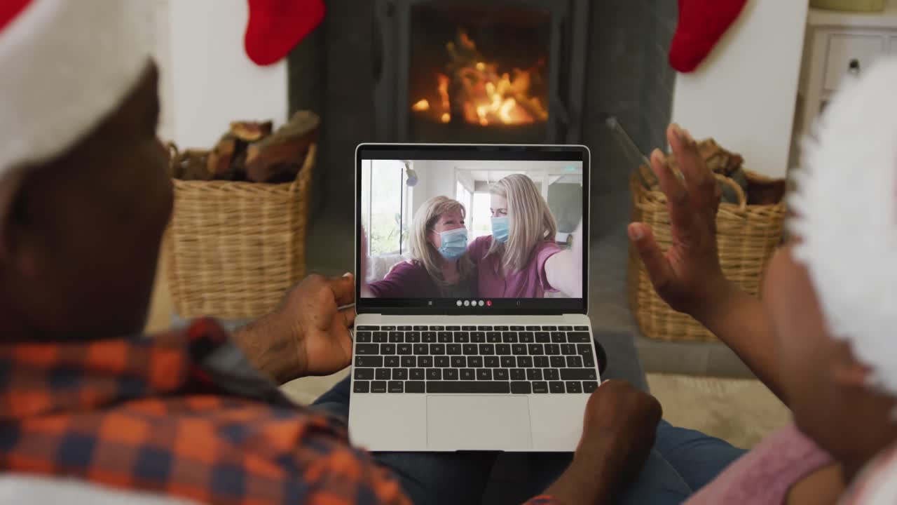 una pareja afroamericana con sombreros de santa usando una computadora portátil para una videollamada de navidad con la familia en la pantalla